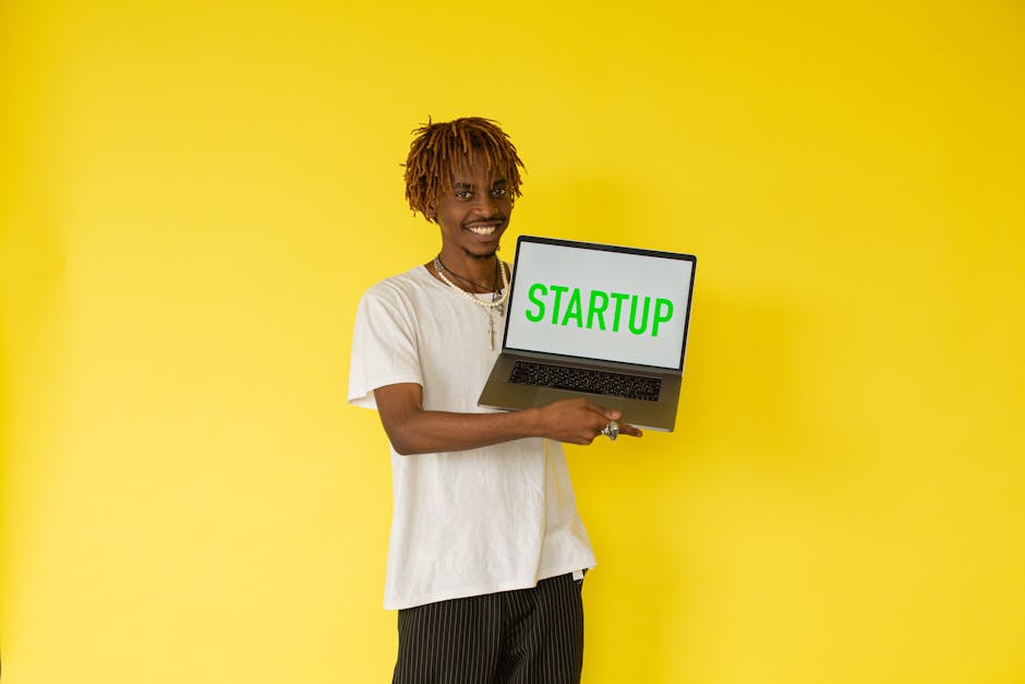Smiling man holding a laptop with 'STARTUP' on screen against vibrant yellow background.