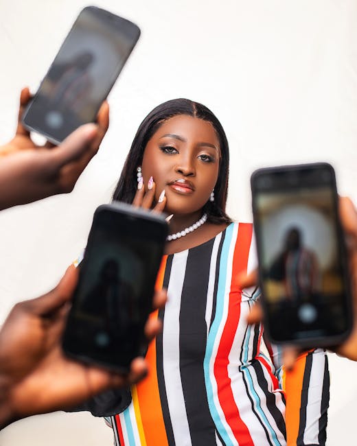Confident woman in striped dress posing for multiple smartphone cameras indoors.