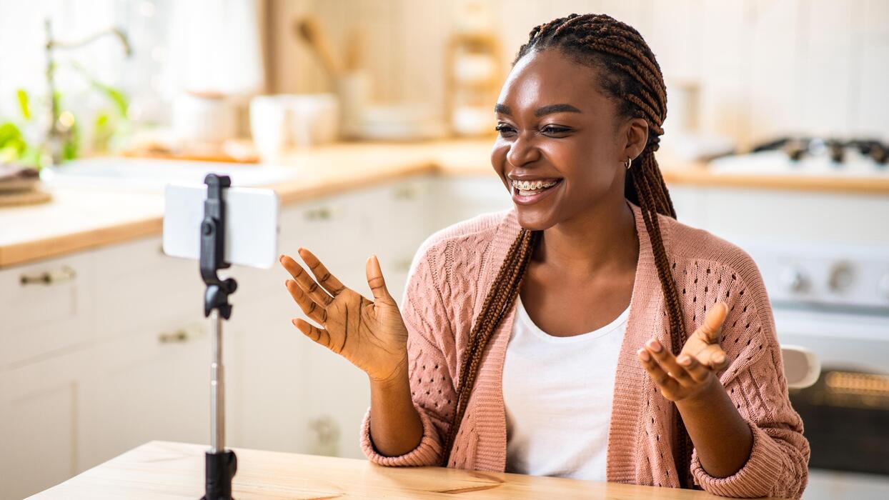 Happy black female recording content for her vlog, using smartphone on  tripod while sitting in kitchen at home, cheerful african blogger woman  influencer talking at camera, making live stream 68496772 Stock Photo
