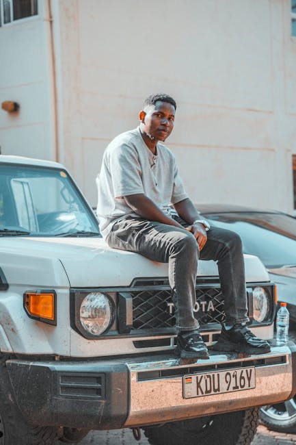 A young man seated casually on an SUV in an urban setting in Nairobi, Kenya.