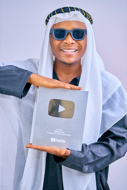 Smiling man in sunglasses and traditional attire holding an award plaque indoors.