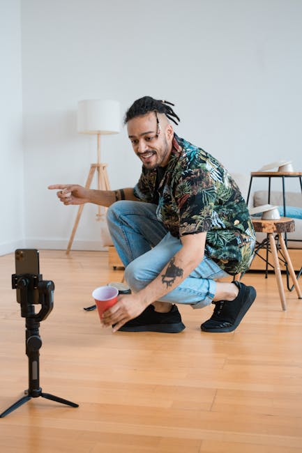 Man in casual outfit filming content with smartphone and tripod indoors.