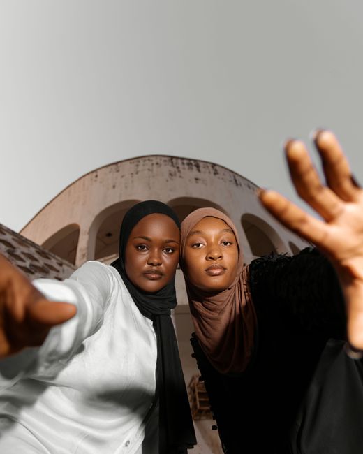 Two young women in hijabs pose confidently in front of Abuja's modern architecture.