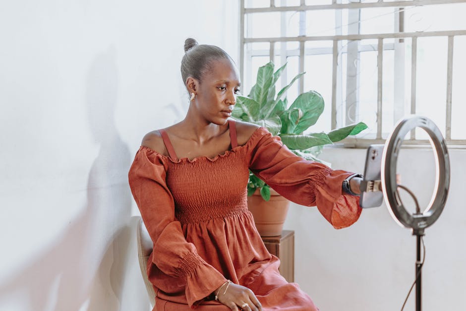 Portrait of a young woman using a smartphone and ring light indoors, Abuja.