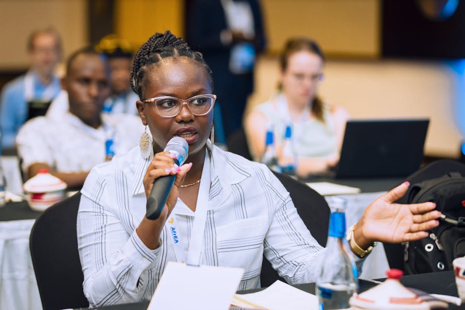 Woman speaking into a microphone during a business conference, engaging with audience.