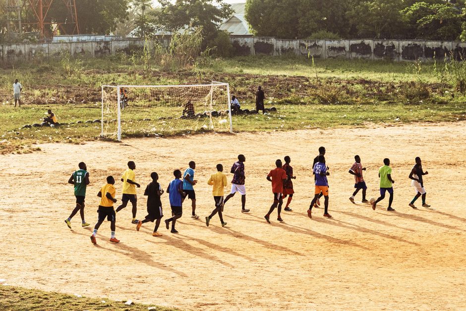 A group of young men practicing soccer on a dirt field under the sun.