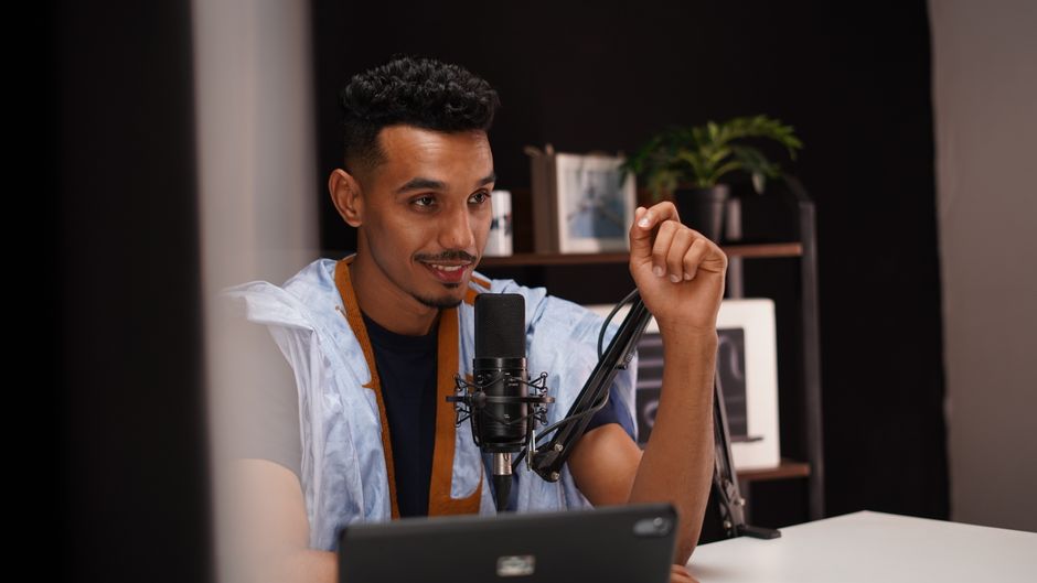 Confident young man speaking into a microphone during a podcast recording in a modern studio.