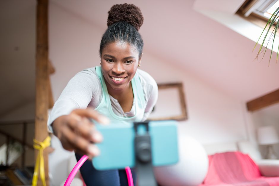 A cheerful woman in workout gear films a fitness video indoors, capturing positive energy.