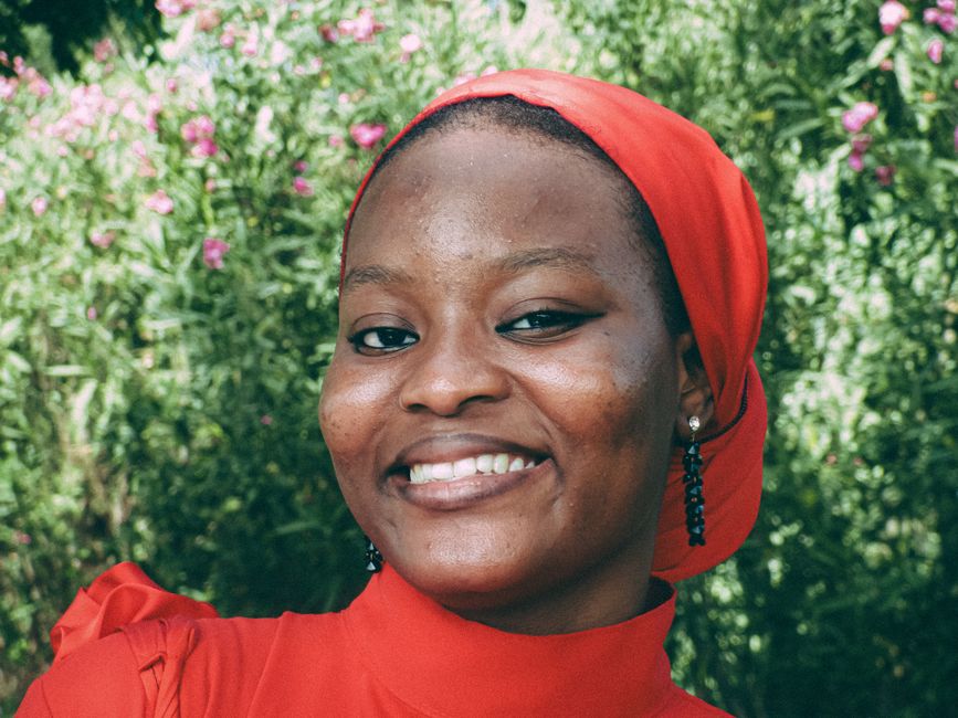 Portrait of a smiling woman in a vibrant red headscarf amidst a lush garden in Tangier, Morocco.