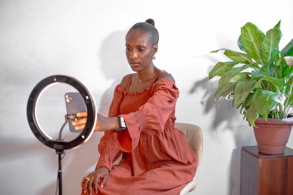 A young woman uses a smartphone and ring light for vlogging indoors.