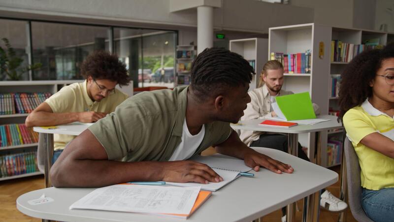 Four multiracial students studying learning education together in classroom high school university college writing in copybook lesson African man guy ask help to American woman girl discuss exercise 67792434 Stock Video at