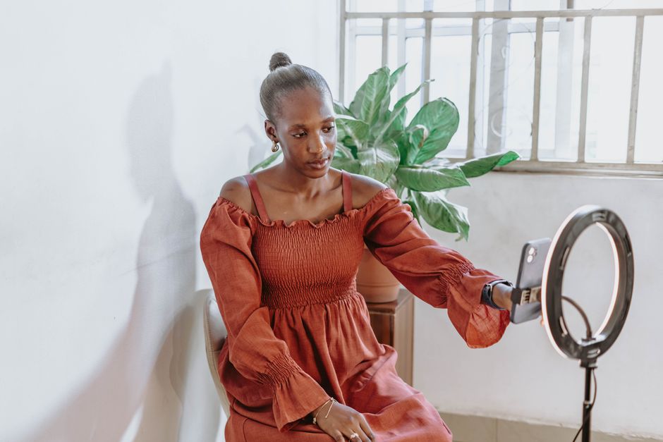 Fashionable woman vlogging indoors with ring light and phone in Abuja, Nigeria.