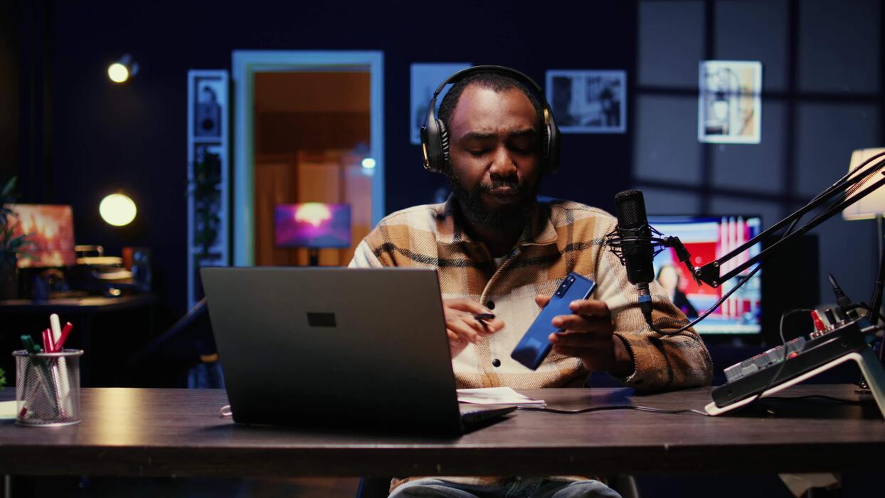 Portrait of african american tech expert reviewing newly released smartphone in rgb lights living room studio. Entertaining influencer filming technology channel vlog using professional camera