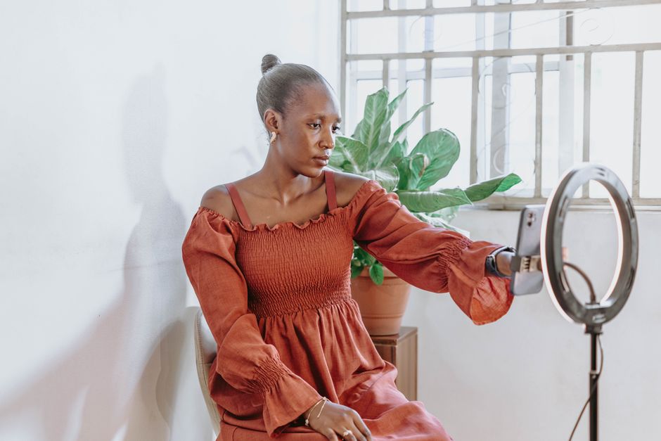 Portrait of a young woman using a smartphone and ring light indoors, Abuja.